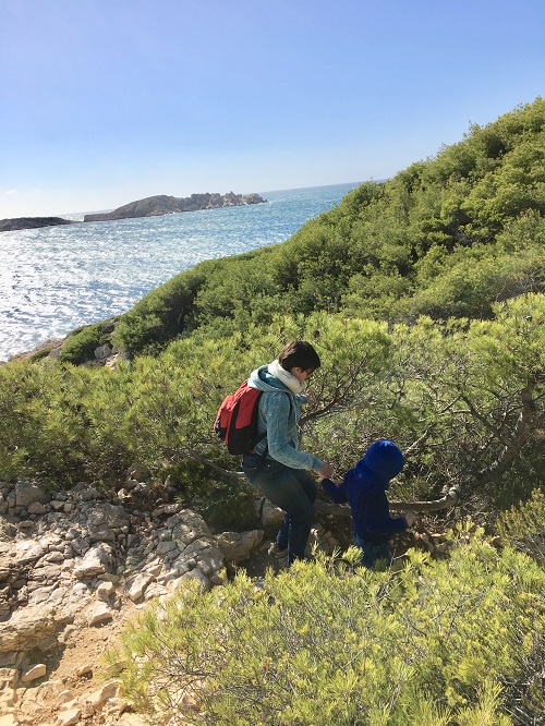 Une mere et son enfant marchant au bord de mer, sous les pins