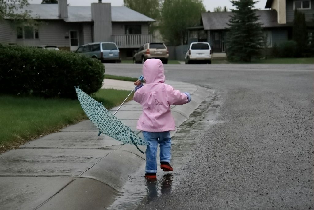 Jeune enfant en veste de pluie rose tenant un parapluie sur un trottoir mouillé